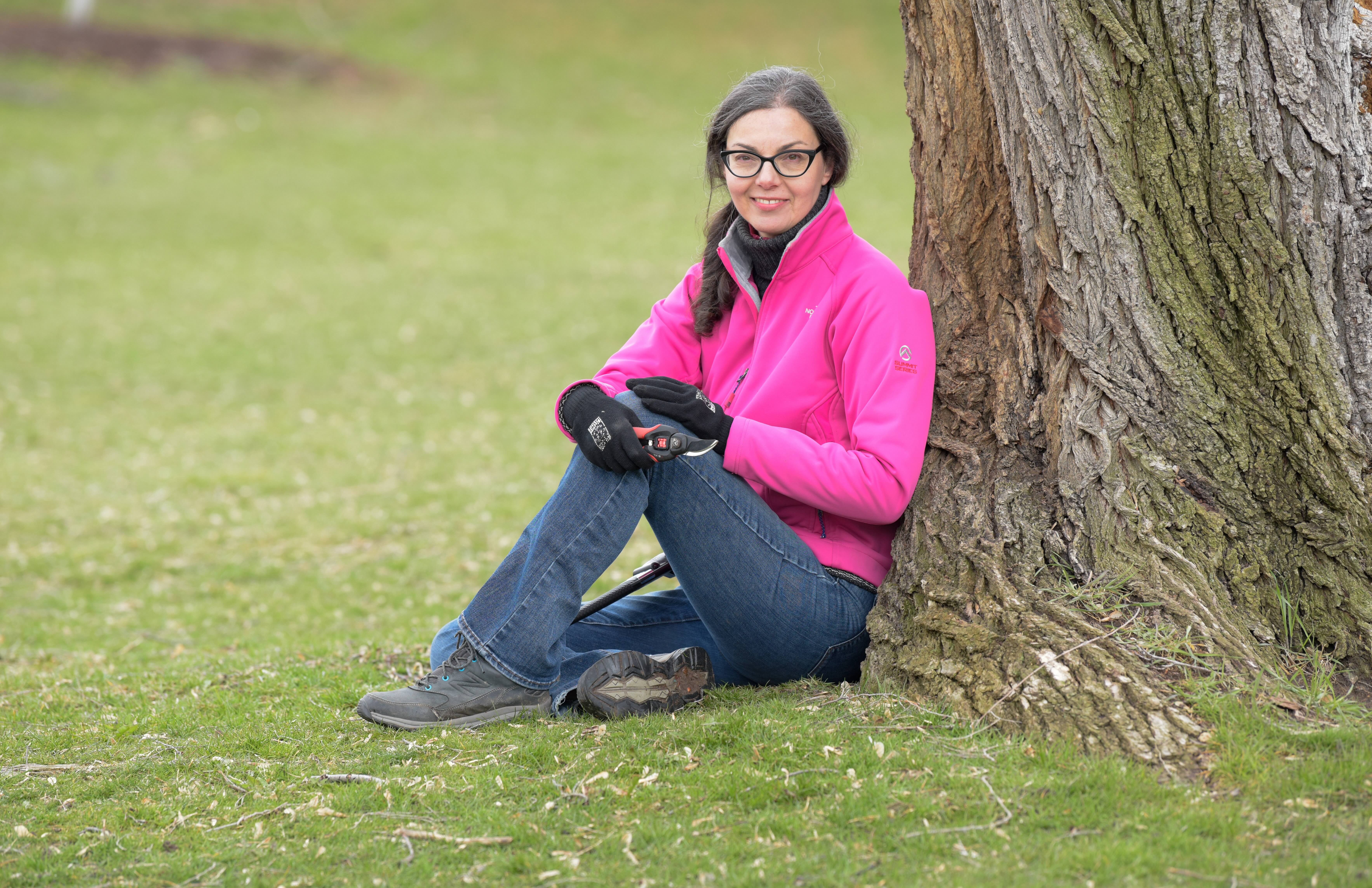 Susan Poizner of OrchardPeople.com sitting by a tree with hand pruners in hand